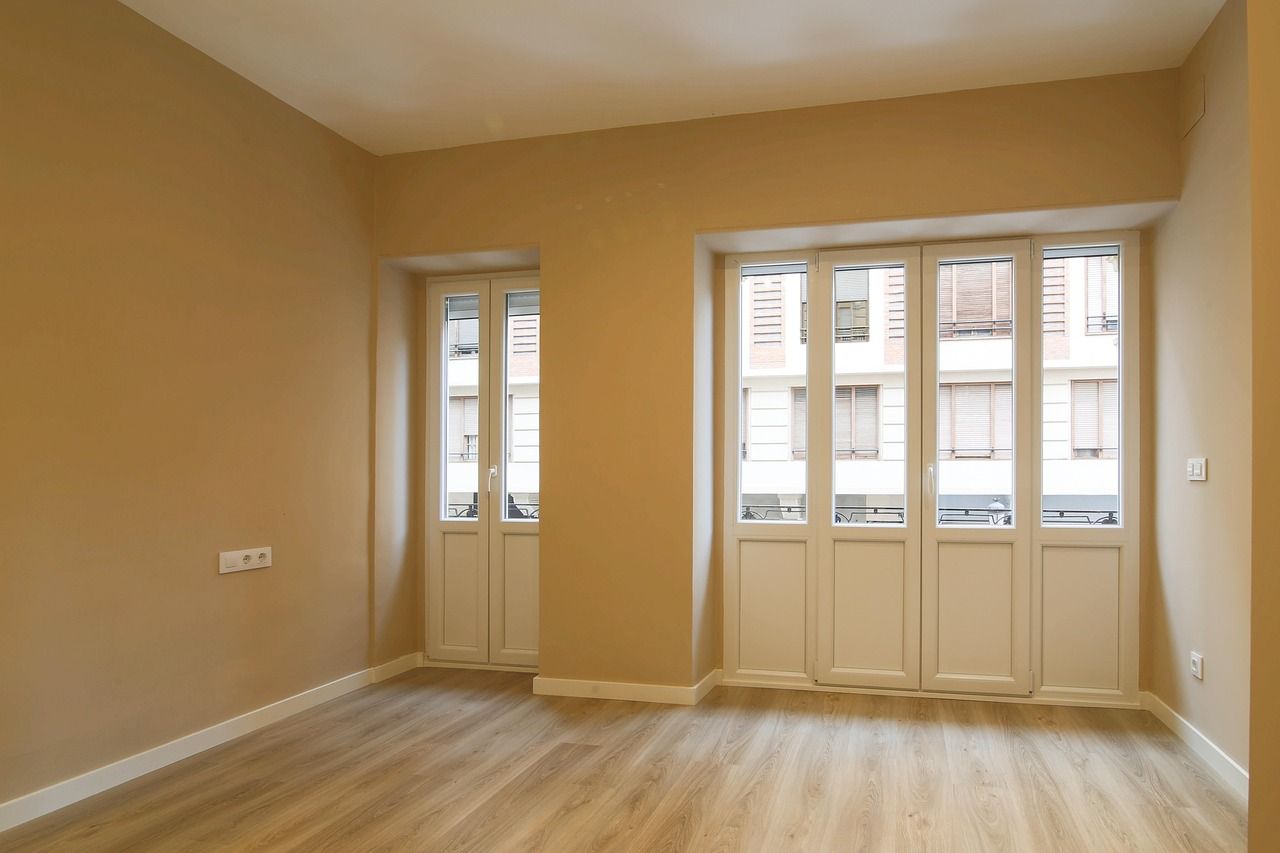 Salón vacío y recién pintado con suelo de madera y balcones a la calle: qué necesito para alquilar mi piso antes de enseñarlo